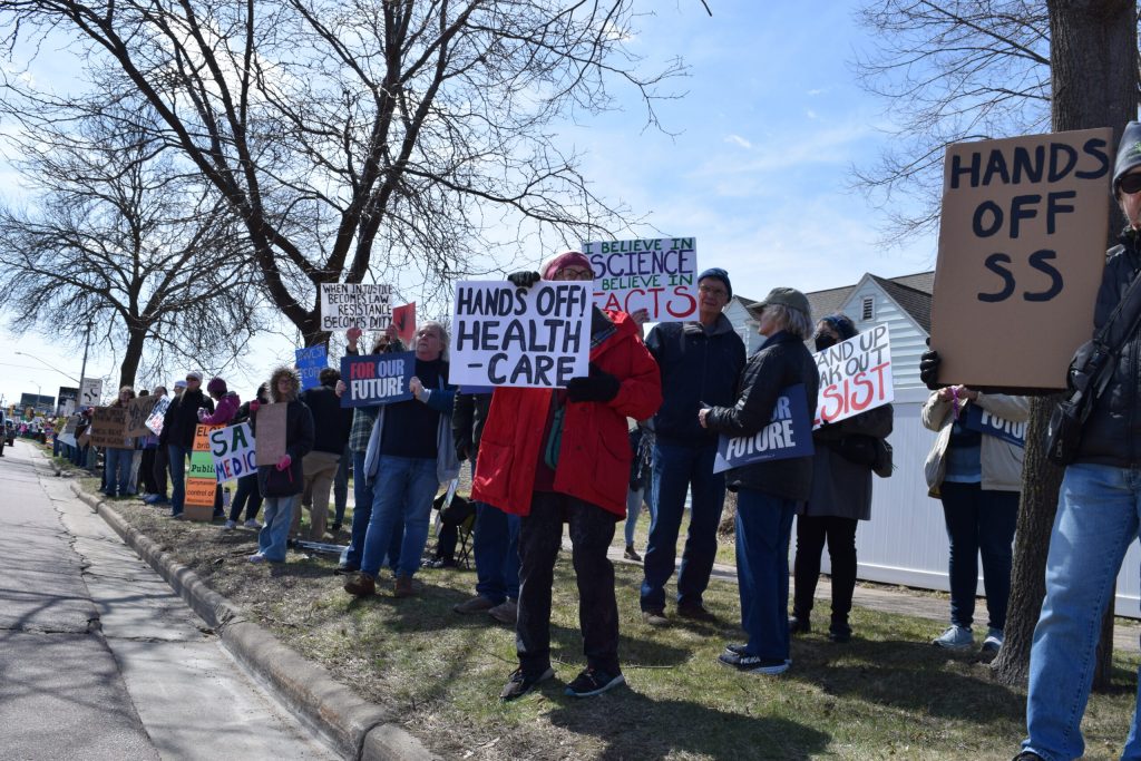 Hundreds of protesters lined a busy intersection in La Crosse, Wis. to protest federal layoffs and funding cuts under the Trump administration on Saturday, April 5, 2025. Hope Kirwan/WPR
