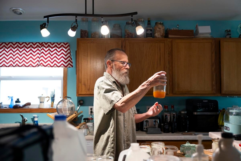 Earl Lowrie pours a glass of the kombucha he’s been fermenting in the kitchen at his home, June 21, 2025, in Cameron, Wis. Lowrie, who has struggled with depression and suicidal thoughts throughout his life, sees a therapist he found after calling the National Alliance on Mental Illness (NAMI) hotline and getting connected to the organization’s Chippewa Valley local affiliate in Wisconsin. (Joe Timmerman / Wisconsin Watch)