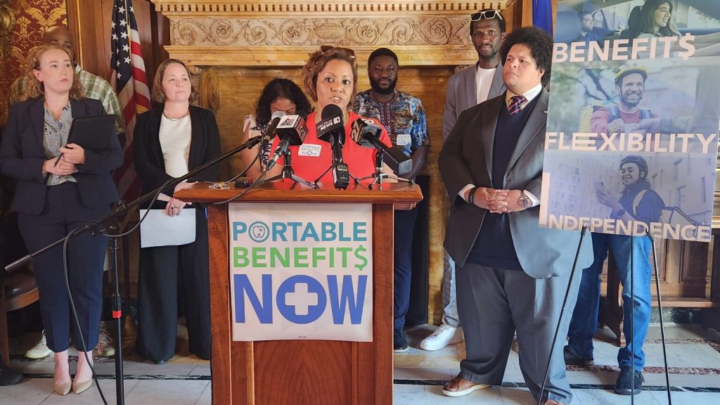 At a news conference Tuesday in the state Capitol, Rachel Smith of New Berlin speaks in favor of a bill that would make app-based drivers independent contractors and allow the businesses they drive for to provide some benefits. The bill was authored by Sen. Julian Bradly, on the right. (Photo by Erik Gunn/Wisconsin Examiner)