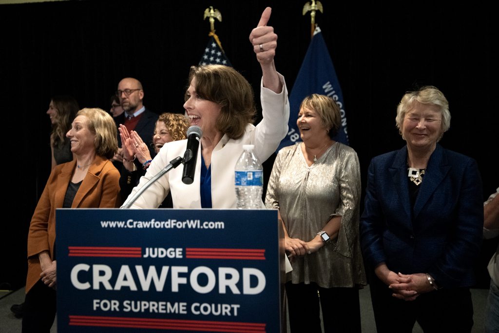Justice Elect Susan Crawford gives a thumbs up to the crowd during her election night speech Tuesday, April 1, 2025, at Park Hotel in Madison, Wis. She is joined by members of the Wisconsin Supreme Court. Angela Major/WPR