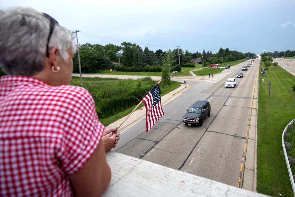 A supporter waves a U.S. flag as a funeral procession for Milwaukee Police Officer Kendall Corder drives by Friday, July 11, 2025, in Brookfield, Wis. Angela Major/WPR