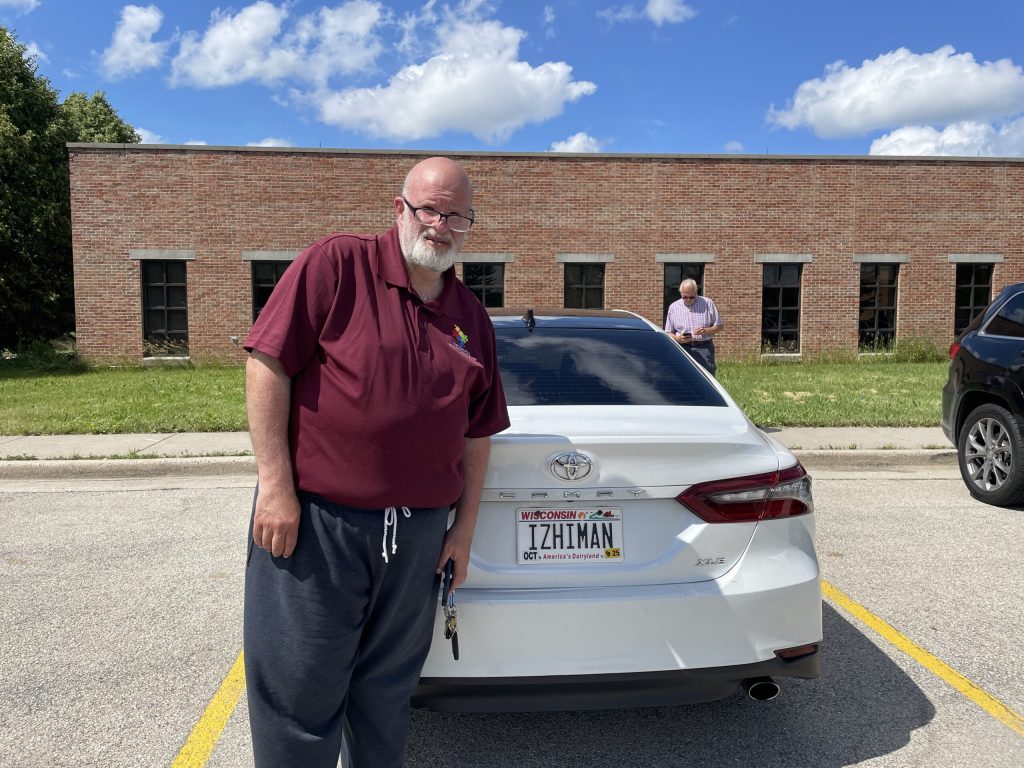 Uber and Lyft driver Yussef Izhiman stands in front of his car at Milwaukee Mitchell International Airport’s rideshare staging lot on June 27, 2025. Nick Rommel/WPR