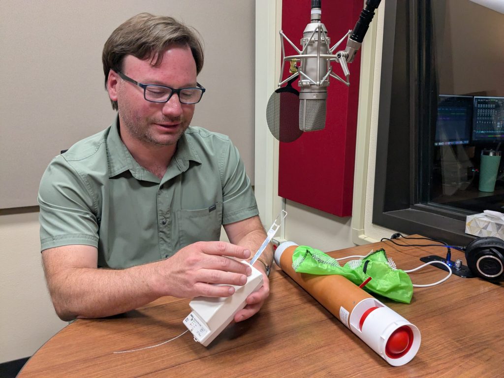 Chris Vagasky holds a radiosonde and explains what it does in the WPR studio on June 23, 2025. Richelle Wilson/WPR