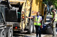 Mayor Cavalier Johnson holds onto a city garbage truck while a skid steer deposits flood debris. Photo by Jeramey Jannene.