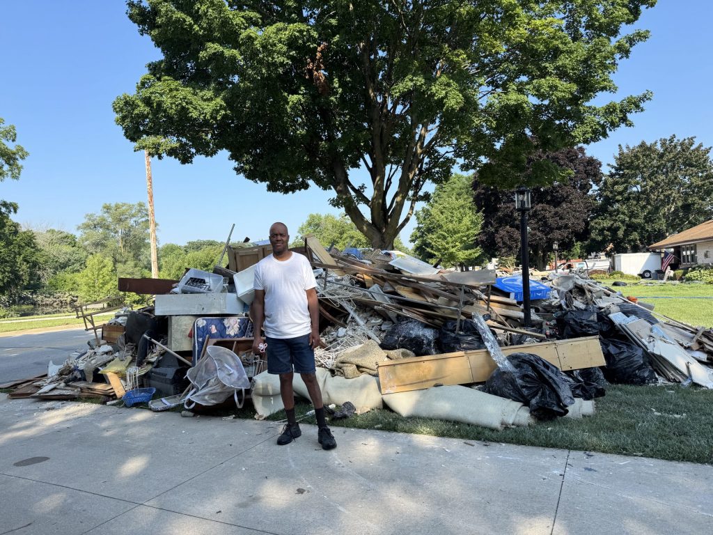 James Moore of Wauwatosa stands in front of damaged items caused by flooding in his basement in August 2025. Evan Casey/WPR