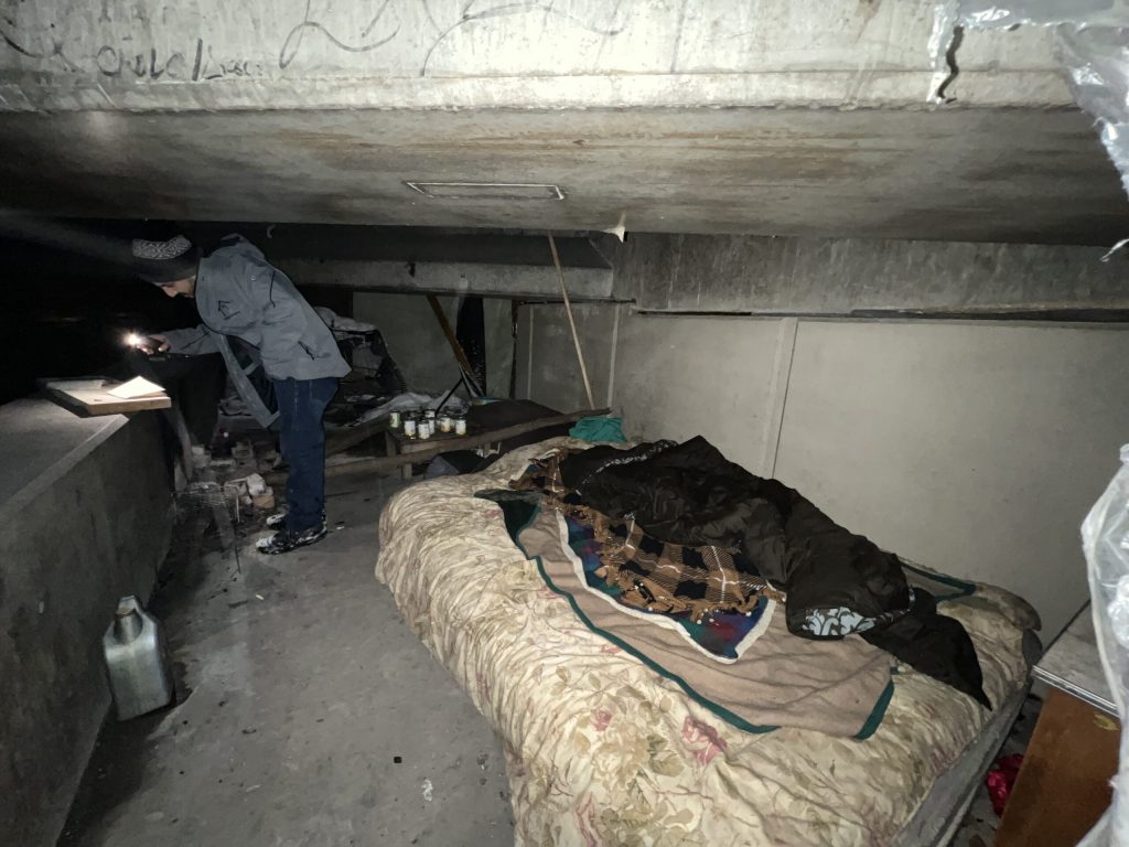 A Milwaukee County homeless outreach worker looks at items underneath a bridge next to Milwaukee’s Kinnickinnic River in January of 2023. Evan Casey/WPR