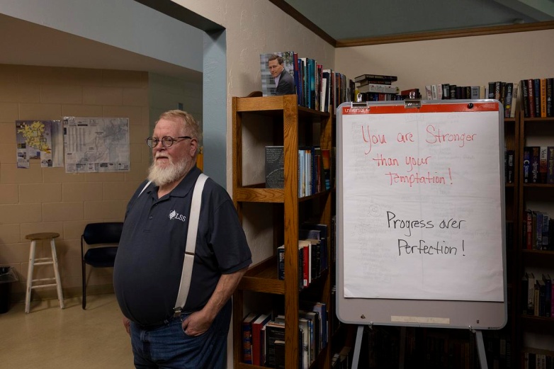 Randy Withrow, site director of Klein Hall, poses for a portrait in front of books stacked on the shelves in the library, Monday, Aug. 25, 2025, at Klein Hall in Chippewa Falls, Wis. (Joe Timmerman / Wisconsin Watch)