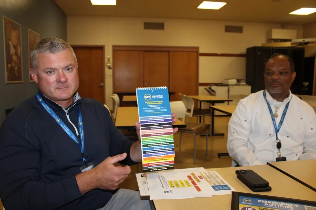 Kevin Hafemann (left) and Shannon Jones, safety personnel at Milwaukee Public Schools, discuss the district’s new Standard Response Protocol. Hafemann shows the emergency-related materials previously available at MPS, saying that the new material is easier to use in an actual emergency. (Photo by Devin Blake)