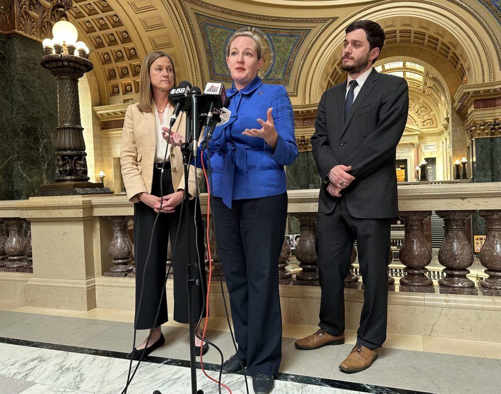 Sen. Kelda Roys, D-Madison, center, speaks at a press conference flanked by Rep. Deb Andraca, D-Whitefish Bay, left, and Rep. Tip McGuire, D-Kenosha, right, at the Wisconsin State Capitol on June 19, 2025. Anya van Wagtendonk/WPR