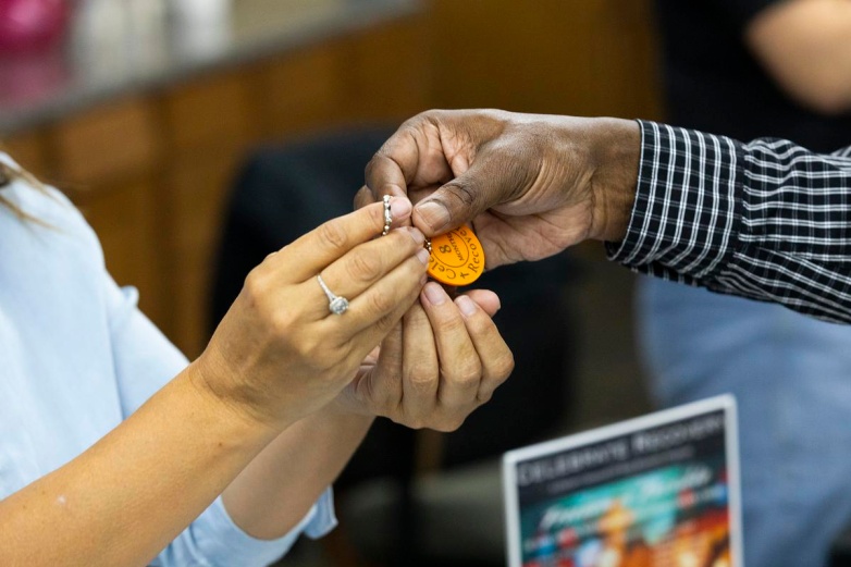 Darnell Price, right, is handed a token celebrating his eight months in recovery during a Home to Stay resource fair for people reentering society after incarceration, Oct. 1, 2025, at Community Warehouse in Milwaukee. “In treatment, I started feeling better and better until finally, the lights started coming back,” Price says. (Joe Timmerman / Wisconsin Watch)