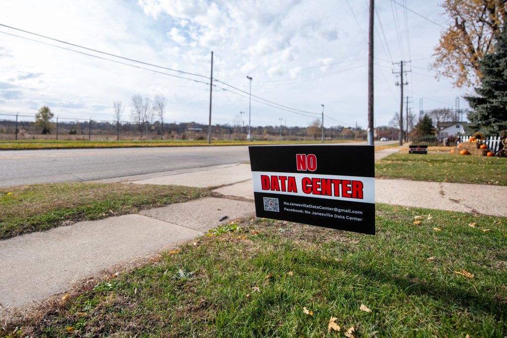 A sign advocating against a proposed data center is displayed in the lawn of a home located across the street from the former Janesville GM Assembly Plant on Tuesday, Nov. 11, 2025, in Janesville, Wis. Angela Major/WPR