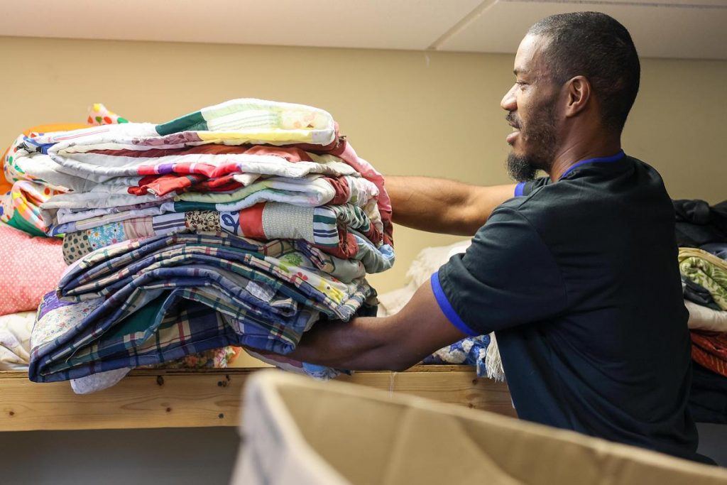 Darren Ingram, a staff member at Repairers of the Breach, stocks quilts on a shelf. Photo from NNS.