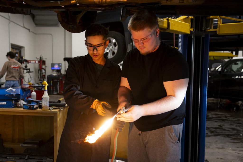 Edduar Beperec, left, and Lucas Pearl adjust the valves of an oxygen-acetylene torch while working on a car during an Auto 3 dual enrollment class on Nov. 12, 2025, at Vel Phillips Memorial High School in Madison, Wis. Students who pass the course earn five Madison College credits for free and skip the class if they enroll at the college. (Joe Timmerman / Wisconsin Watch)