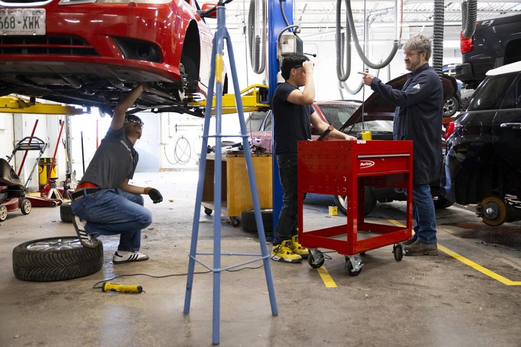 Oscar Haro Rodriguéz, left, works on a car as José Ruiz, center, talks to their teacher, Miles Tokheim, during an Auto 3 dual enrollment class on Nov. 12, 2025. (Joe Timmerman / Wisconsin Watch)