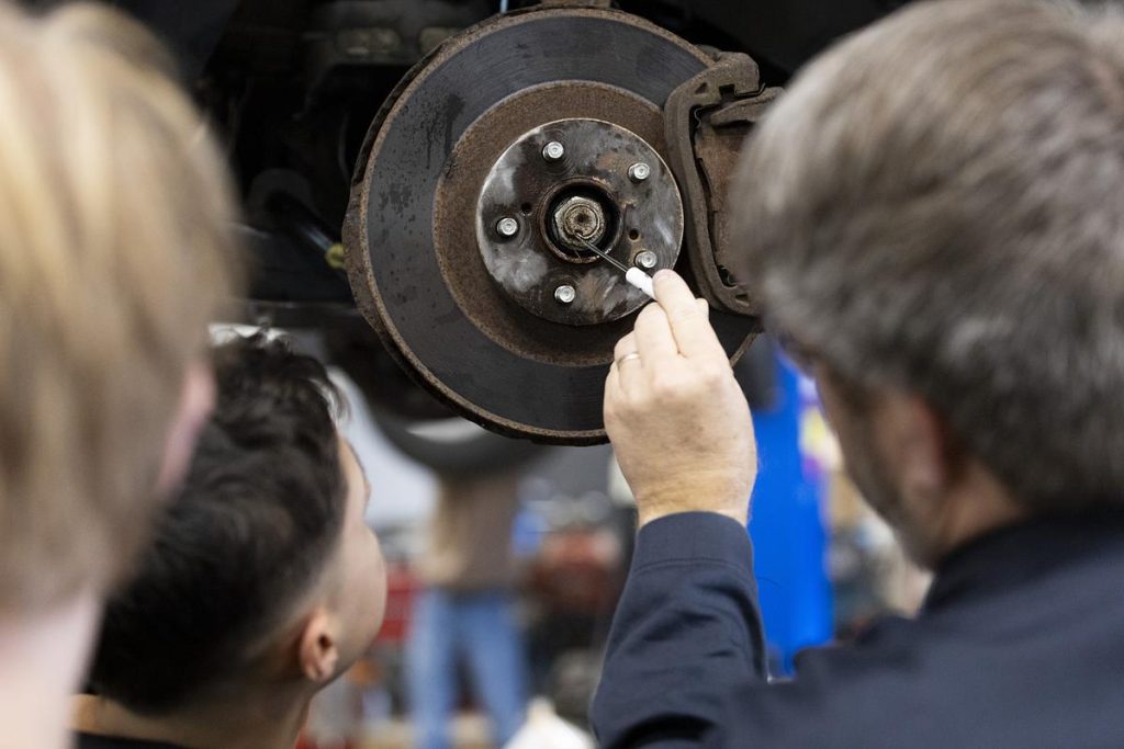Miles Tokheim, right, helps his students work on a car during an Auto 3 dual enrollment class on Nov. 12, 2025. Small, urban or high-poverty schools are least likely to offer dual enrollment classes, a Wisconsin Policy Forum analysis shows. (Joe Timmerman / Wisconsin Watch)