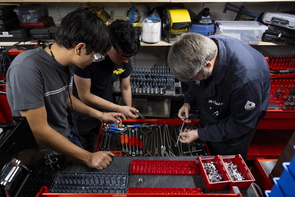 Oscar Haro Rodriguéz, left, and José Ruiz, center, look for a tool with their teacher, Miles Tokheim, during an Auto 3 dual enrollment class on Nov. 12, 2025. Tokheim met Madison College’s requirements to teach dual enrollment since he is a certified auto service technician with a master’s degree. (Joe Timmerman / Wisconsin Watch)
