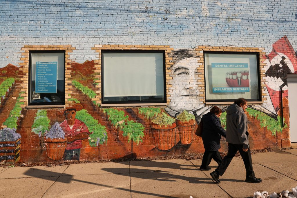 A couple walks past a mural of Cesar Chavez on the side of a building at 1037 S. Cesar E. Chavez Drive. (Photo by Jonathan Aguilar / Milwaukee Neighborhood News Service / CatchLight Local)
