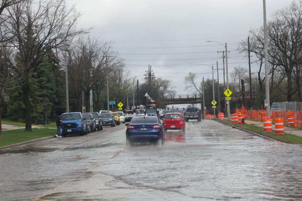 Cars drive through a flooded South 43rd Street across from Jackson Park, heavy rainfall caused flooding throughout Milwaukee. Heavy rainfall and flooding could hit the area again later this week. (Photo by Jonathan Aguilar / Milwaukee Neighborhood News Service / CatchLight Local)