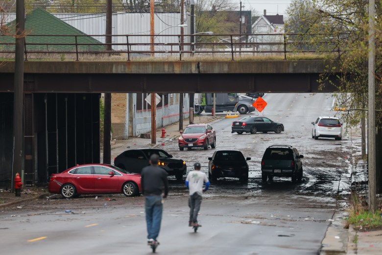 People ride scooters toward several stuck cars underneath the railroad crossing bridge on West Burleigh Street after heavy rainfall caused flooding throughout Milwaukee on April 16. (Photo by Jonathan Aguilar / Milwaukee Neighborhood News Service / CatchLight Local)