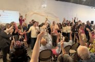 Katie Cummings (center), founder of Pink Umbrella Theater Co., holds up large scissors after cutting the ribbon at the organization's new theater on June 7. (Photo by Jake Dale / Milwaukee Neighborhood News Service)