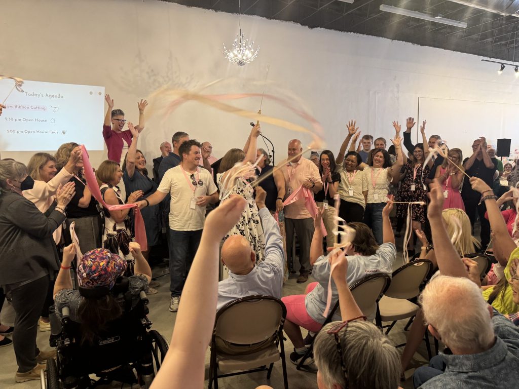 Katie Cummings (center), founder of Pink Umbrella Theater Co., holds up large scissors after cutting the ribbon at the organization's new theater on June 7. (Photo by Jake Dale / Milwaukee Neighborhood News Service)