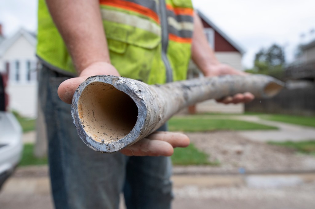 An engineering technician with the city of Milwaukee holds up a replaced lead service line on June 29, 2021. (Isaac Wasserman / Wisconsin Watch)