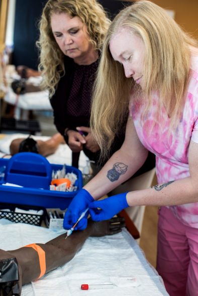 Violet LaClair practices drawing blood from a mannequin arm while Lisa Fahey, manager of Ambulatory Apprenticeships, observes. (Narayan Mahon for Wisconsin Watch)