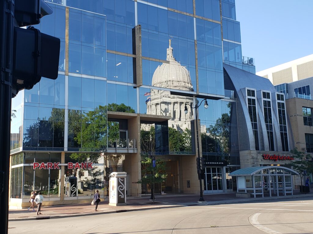 The Wisconsin State Capitol reflected in the glass windows of Park Bank on the Capitol Square in Madison. (Wisconsin Examiner photo)