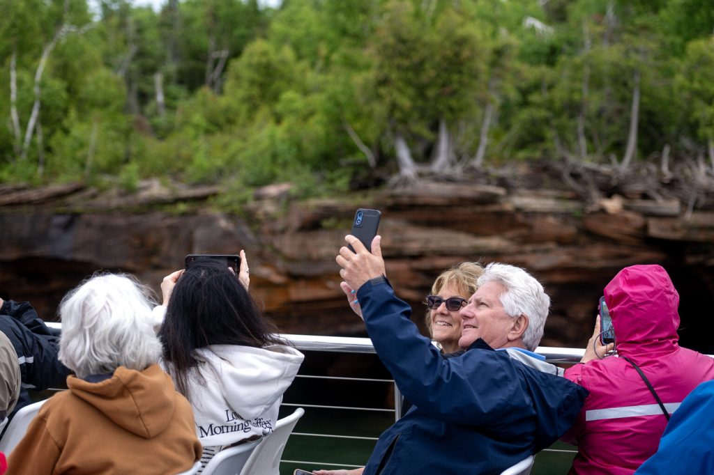 People take photos as they pass by the Apostle Islands on Wednesday, July 8, 2026, in Bayfield, Wis. Angela Major/WPR