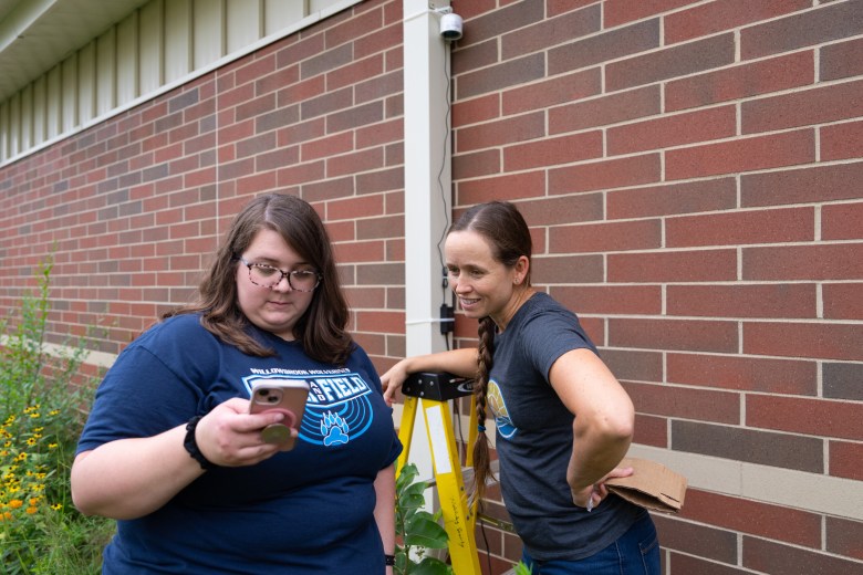 Fifth grade science teacher Erika Goodsell, left, and Brittany Keyes, clean air policy manager for Healthy Climate Wisconsin, right, look at the air quality reading from a PurpleAir air quality sensor at Willowbrook Middle School in South Beloit, Illinois, on Aug. 14, 2026. (Kayla Wolf for Wisconsin Watch)