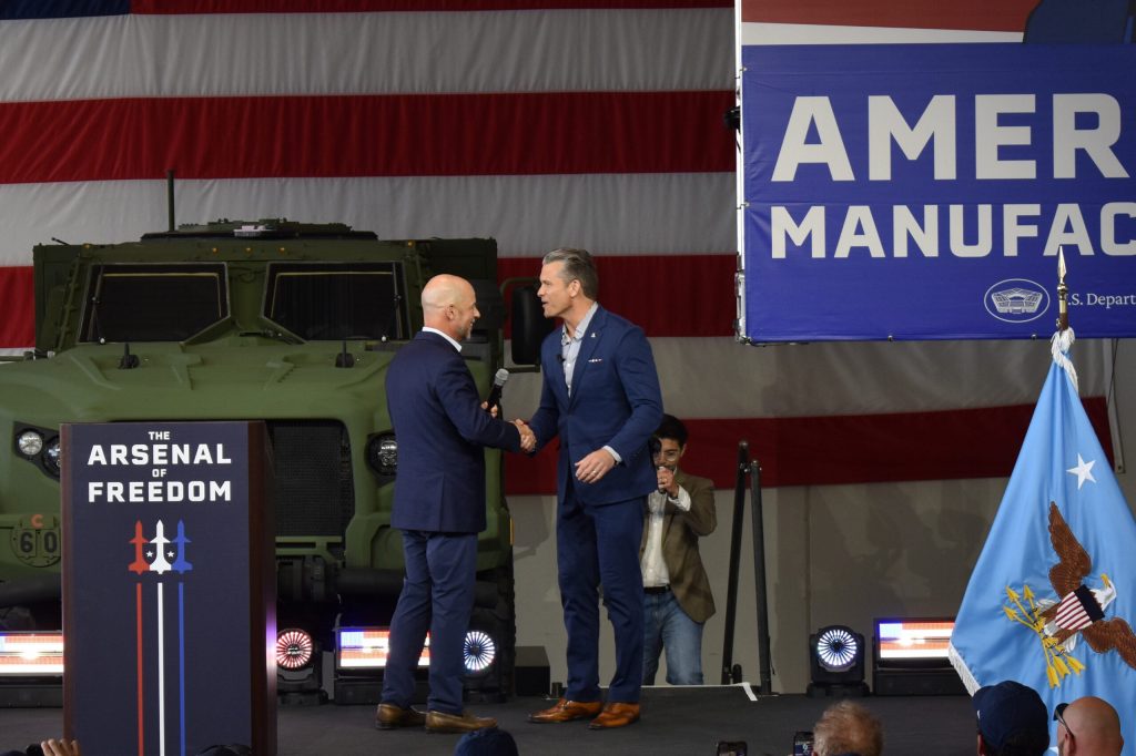 U.S. Defense Secretary Pete Hegseth, right, shakes hands with Oshkosh Corp. CEO John Pfeifer at an event in Oshkosh, Wis., on Aug. 24, 2026. Joe Schulz/WPR