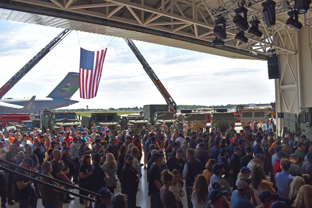 A crowd of Oshkosh Corp. employees stands in an airplane hangar at the Wittman Regional Airport in Oshkosh, Wis., waiting for U.S. Defense Secretary Pete Hegseth’s remarks. Joe Schulz/WPR