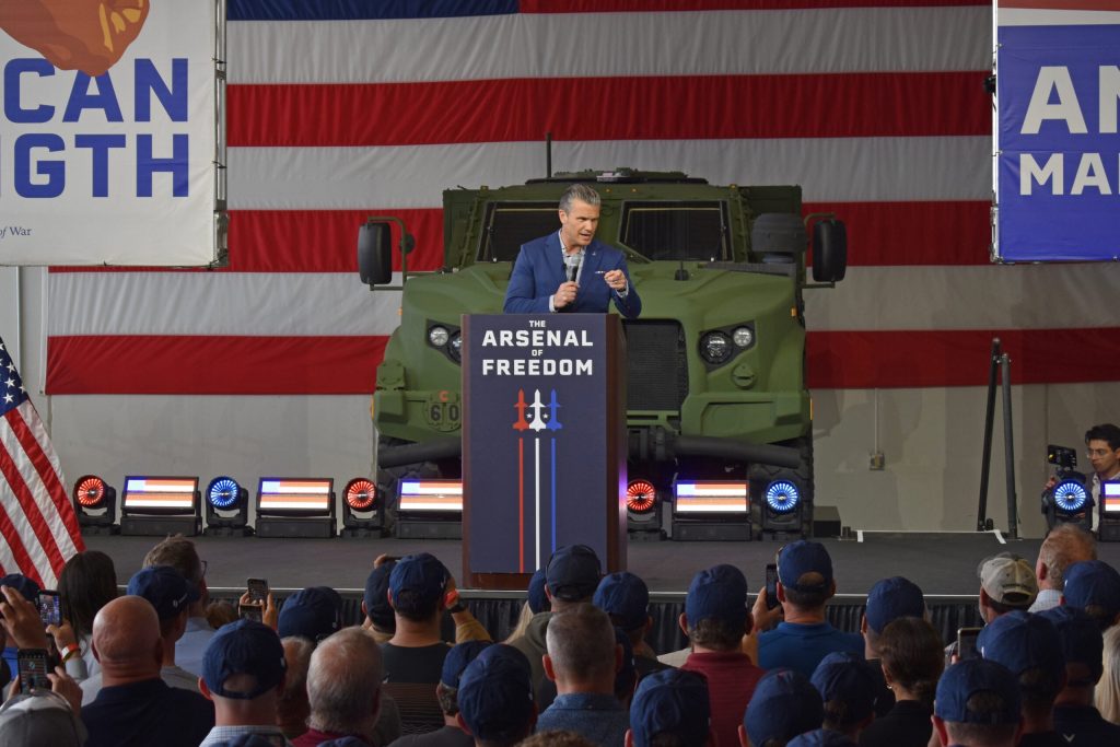 U.S. Defense Secretary Pete Hegseth speaks to a crowd of Oshkosh Corp. workers inside a hangar at the Wittman Regional Airport in Oshkosh, Wis., on Aug. 24, 2026. Joe Schulz/WPR
