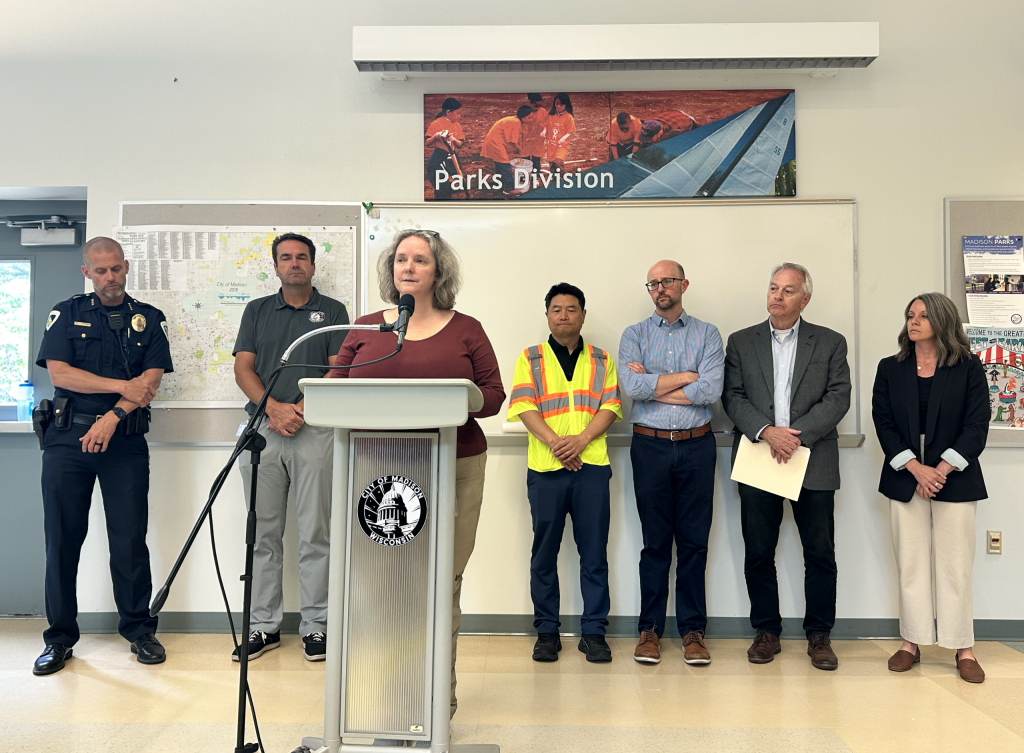 Madison Mayor Satya Rhodes-Conway, flanked by city employees including Police Chief John Patterson, far left, addresses reporters about the Williamson Street protest encampment on Wednesday, Aug. 5, 2026 in Madison, Wis. Anya van Wagtendonk/WPR