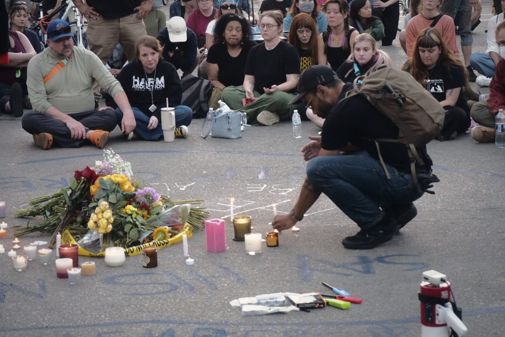 A man crouches to light candles at a memorial site as mourners gather during a vigil at the site where Corey Ruiz was fatally shot by Madison police, July 22, 2026, in Madison, Wis. (Wes Hogg for Wisconsin Watch)