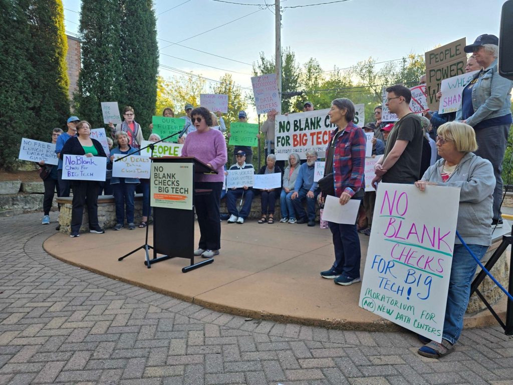 Members of the western Wisconsin community advocacy group GROWW hold a rally in River Falls, Wis. on Sept. 23, 2026, protesting a 2023 tax break, which has since spurred a data center building boom in Wisconsin. The event focused on 30th Assembly District Republican Incumbent Shannon Zimmerman, who authored the legislation. Rich Kremer/WPR
