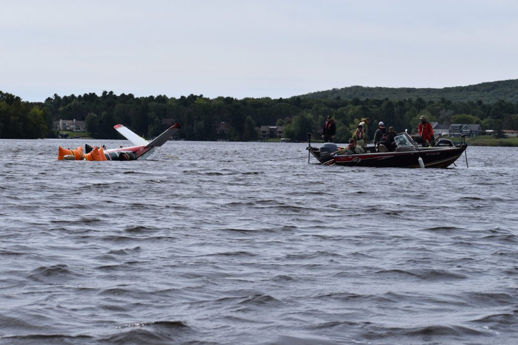 A boat crew nears shore, as more of the aircraft starts to emerge from the lake. Avery Martinez/WPR