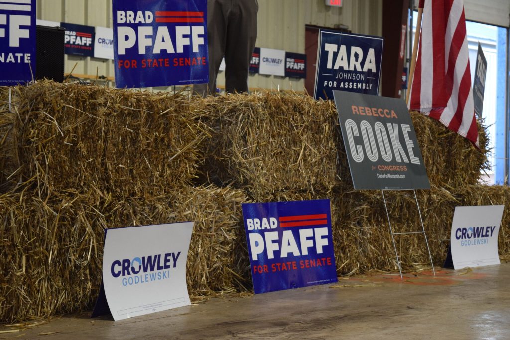 Campaign signs for Democratic candidates line the front of the stage at western Wisconsin Democrats’ annual corn roast on Wednesday, Sept. 2, 2026. Hope Kirwan/WPR
