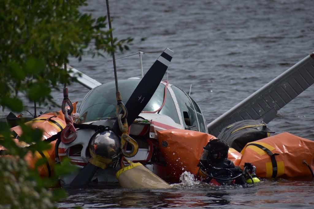 A diver emerges from the water, as they install cables around the wings, fuselage and tail for the crane. Avery Martinez/WPR