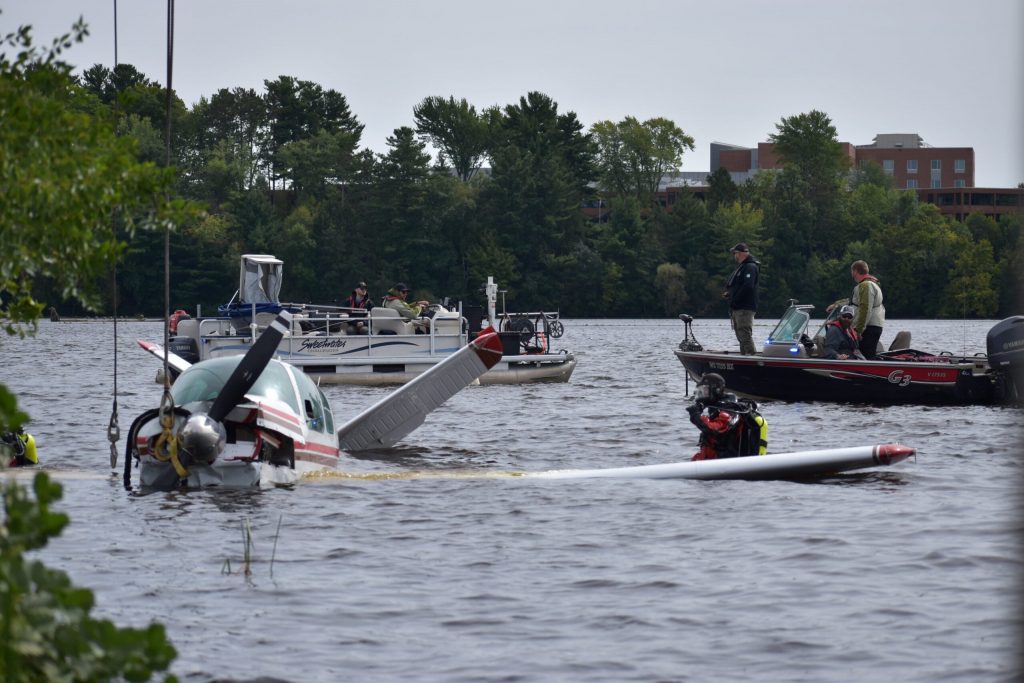 Members of the dive team and other recovery crews watch the plane as the straps are prepared for lifting the aircraft. Avery Martinez/WPR