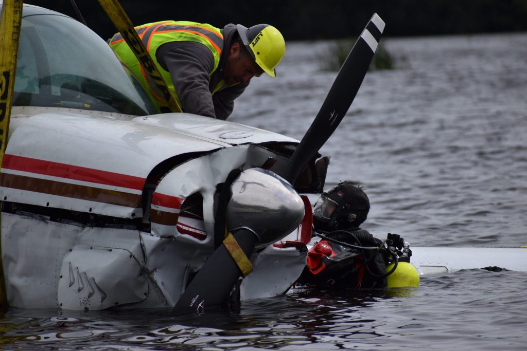A crane operator and diver work above and below sections of the submerged plane, ensuring the cables are secure. Avery Martinez/WPR