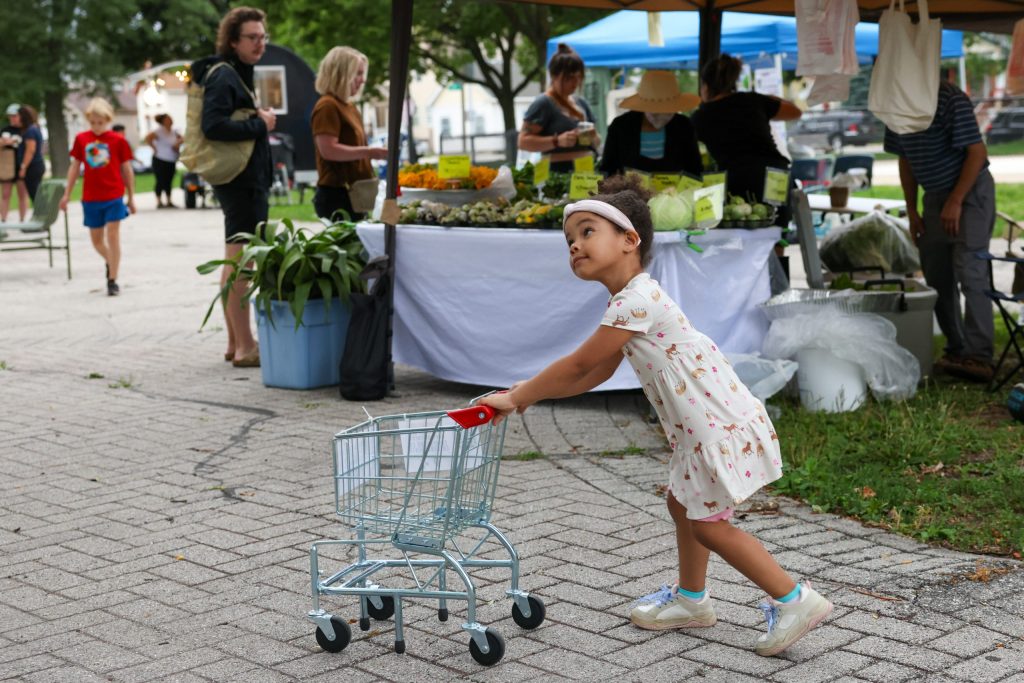 Amanda Nogueras, 4, pushes a shopping cart through the plaza at the Walker Square Farmers Market on Aug. 9. (Photo by Jonathan Aguilar / Milwaukee Neighborhood News Service / CatchLight Local)