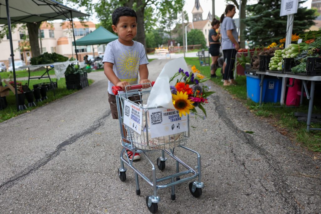 Eli Perez, 3, pushes his shopping cart at Walker Square Park during the Walker Square Farmers Market on Aug. 9. (Photo by Jonathan Aguilar / Milwaukee Neighborhood News Service / CatchLight Local)