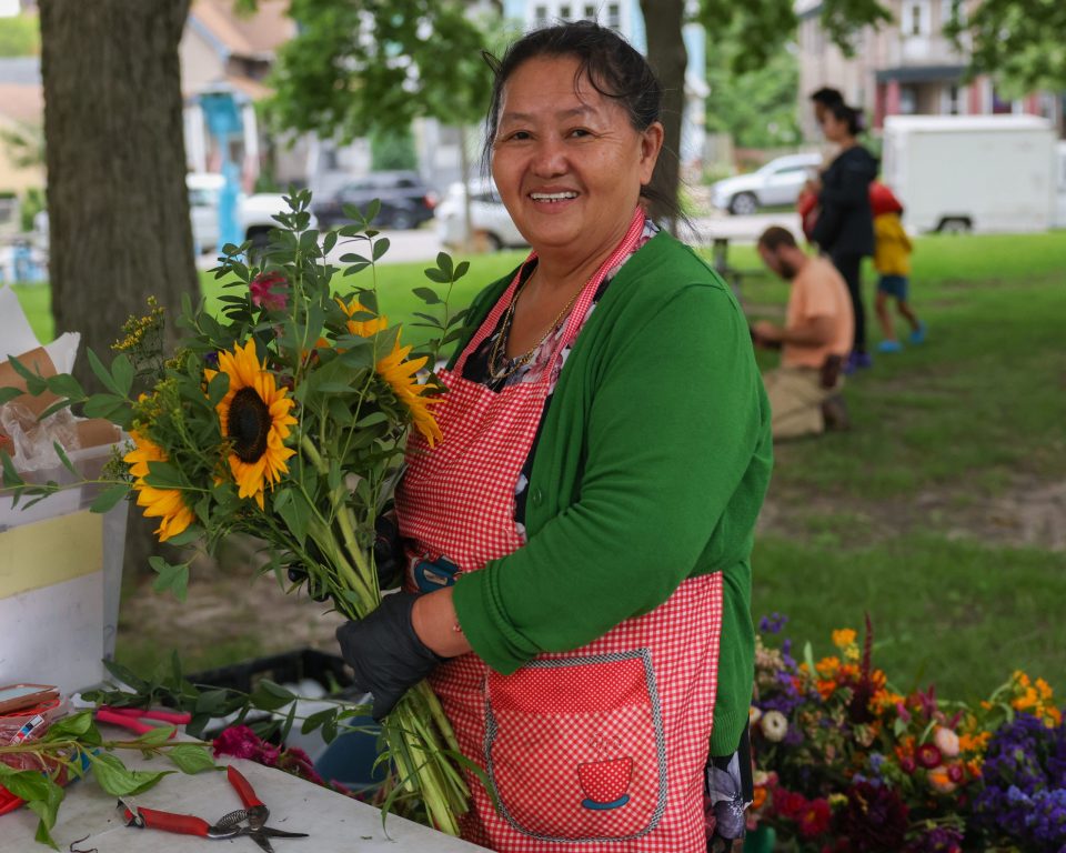 Ue Cheng, florist at Cheng Siong Flowermarket, poses for a portrait with a freshly made bouquet during the Walker Square Farmers Market. (Photo by Jonathan Aguilar / Milwaukee Neighborhood News Service / CatchLight Local)