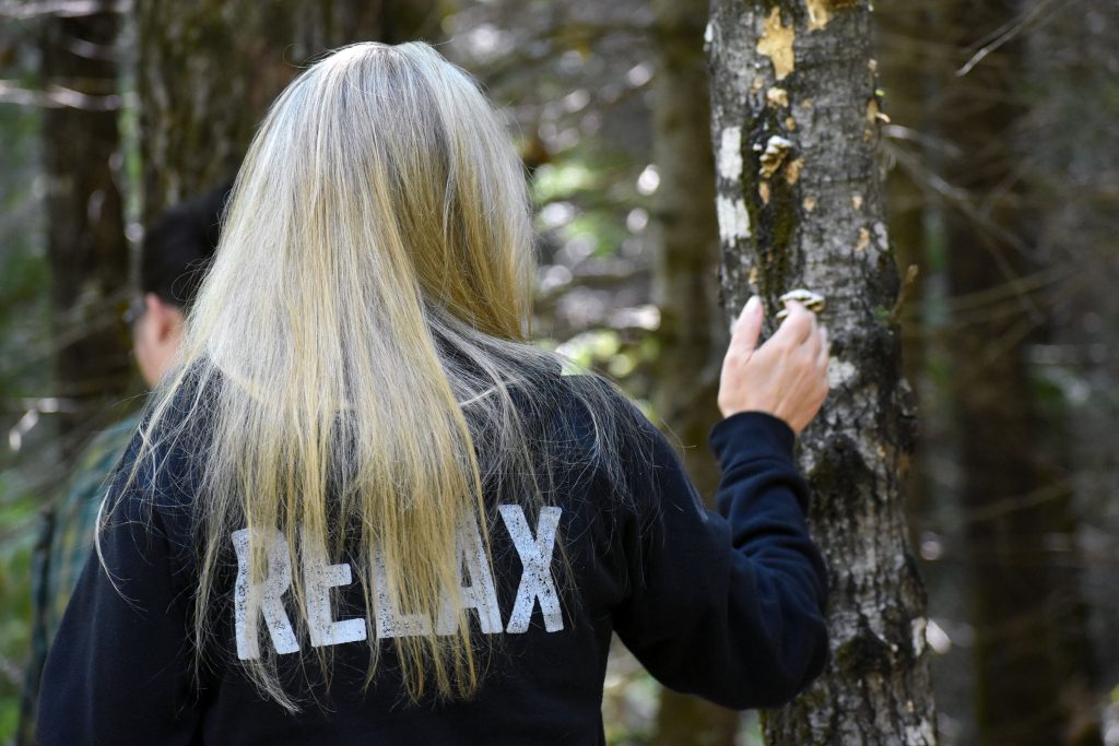 Heather Fletcher of Eagle River touches the bark of a tree during a guided walk on the Tara Lila Forest Bathing Trail on Aug. 8, 2026. Fletcher said she tried forest bathing for the first time after experiencing a stroke and brain aneurysm that ruptured twice in 2022. Danielle Kaeding/WPR