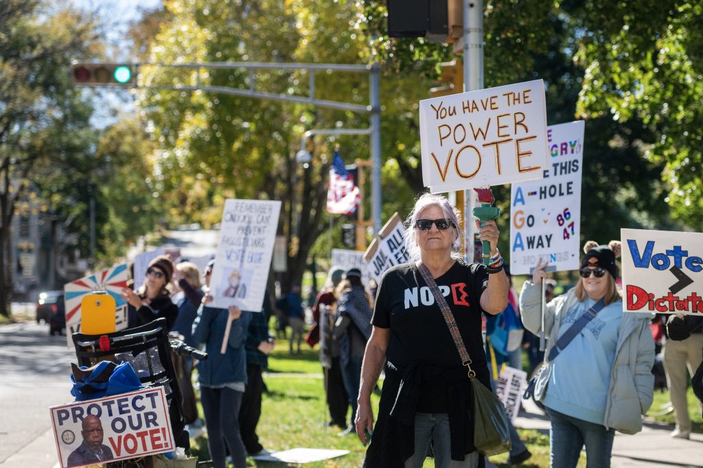 Protesters hold signs at James Madison Park as cars pass by Saturday, Oct. 17, 2026, during a No Kings protest in Madison, Wis. Angela Major/WPR