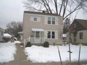 This view affords a glimpse of the accessory entrance to the Larson residence, also affixed with a canopy. Three snow snowshovels, each presumably selected for its distinctive performance attributes, lie at the ready, having clearly done their duty during the recent uncomfortableness. A Christmas wreath bedecking the principal entrance to the residence, was hung in 2013. Twin yellow-topped stakes stabilize a recently planted, city-owned Acer saccharum. Someday in the future, the Larson family can tap their own, sweet, maple syrup.