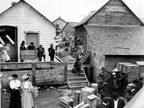 As seen on the official Wikipedia entry (credit: Salvarsan606), this 1912 scene is at the ferry landing where schoolteachers are waiting to go home for the day.