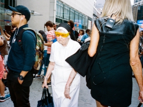 An ill-humored nun presses her way through a throng. She wears yellow fitover sunglasses perched precipitously over her coif and veil, but no glasses under her fitovers.