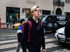 Again on a crosswalk, an otherwise unassuming teenager appears fierce through direct eye contact and a mouth made barbarous by balancing a tripod on his lower lip.